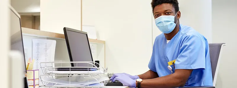 Man in scrubs sitting in a medical office at a computer
